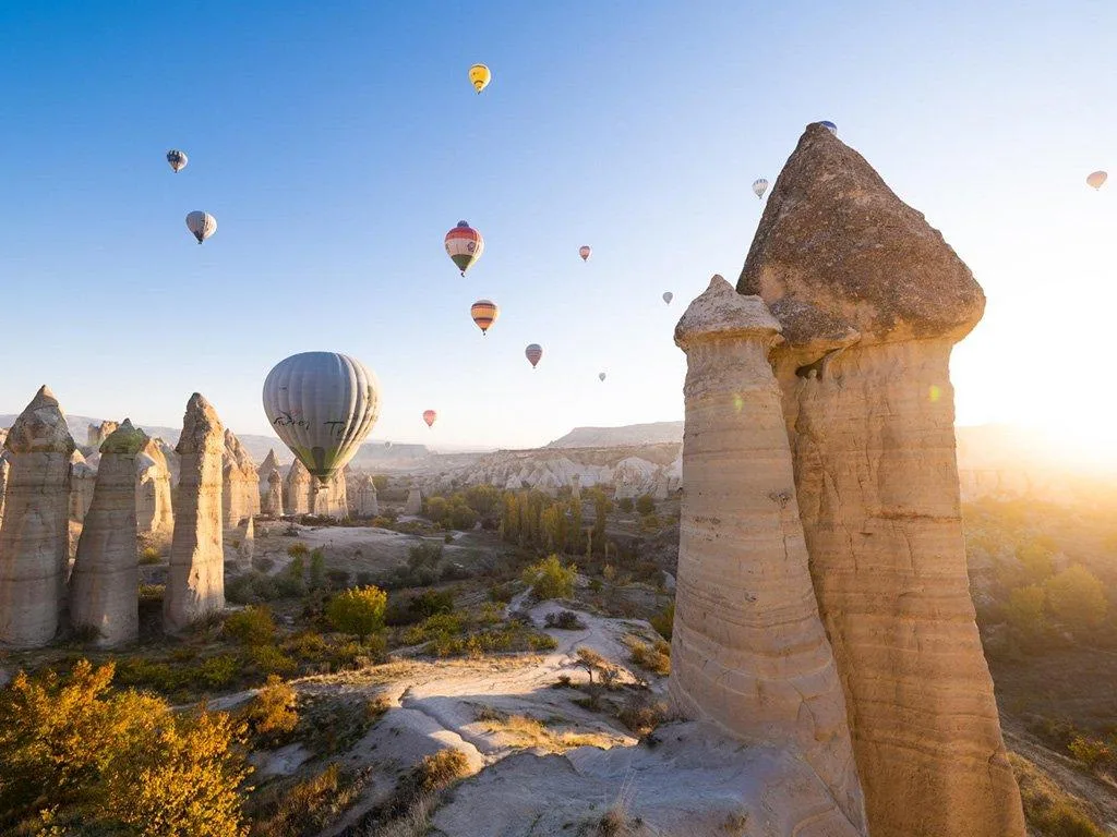 Hot-air balloons rising over rock formations at sunrise in Cappadocia, Türkiye